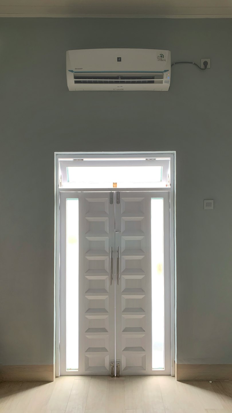 White air conditioner above double doors in a modern room.